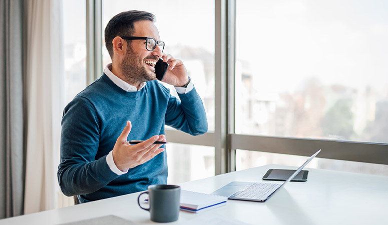 Cheerful businessman talking on smart phone while sitting at off